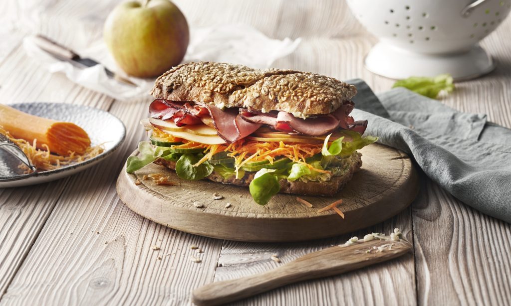 Vollkorn Stange mit Schinken Apfel und Möhre auf einem Holzbrett