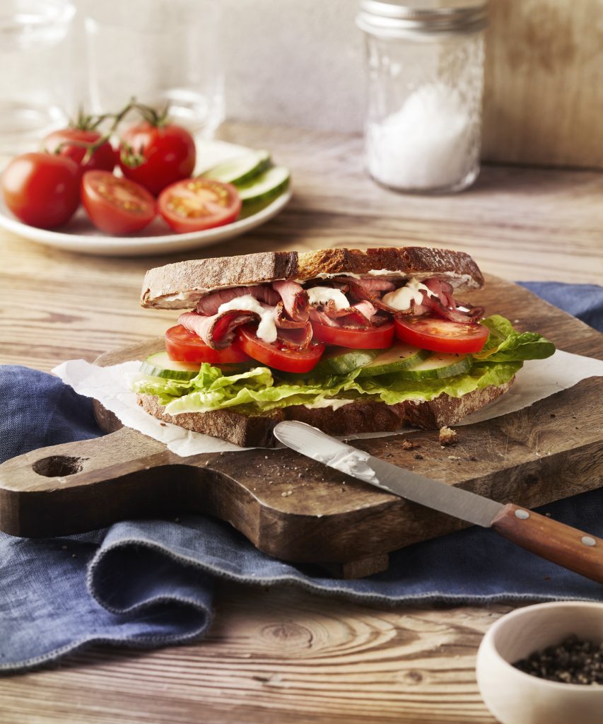 Belegtes Brot mit Tomaten Gurke und Roastbeef auf Holzbrett